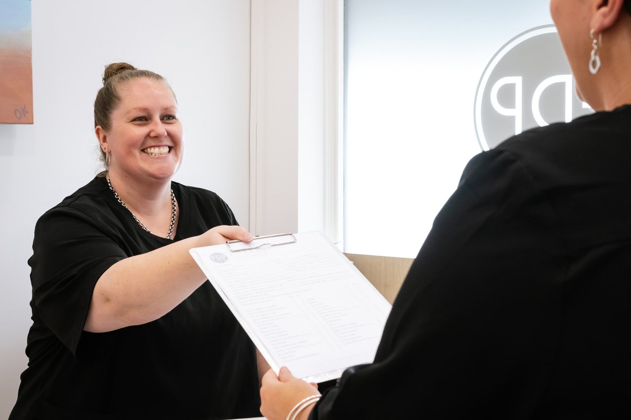 A smiling receptionist handing a form across the front desk at Flinders Dental Practice